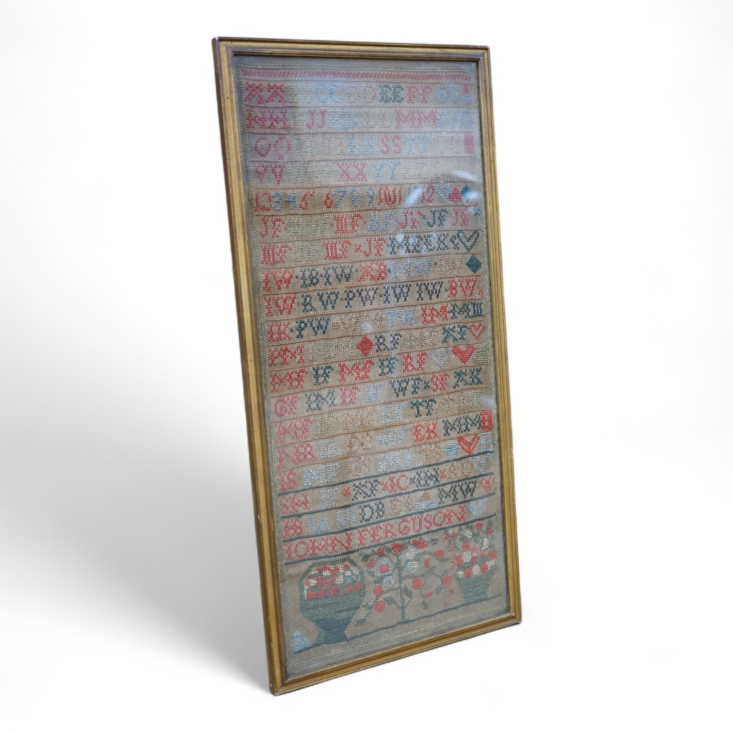 A 19th century cross stitch alphabet sampler, dated 1825 by John Ferguson. Worked in rows of letters and numerals, with a panel embroidered with a basket and vase of flowers. 43 x 19cm